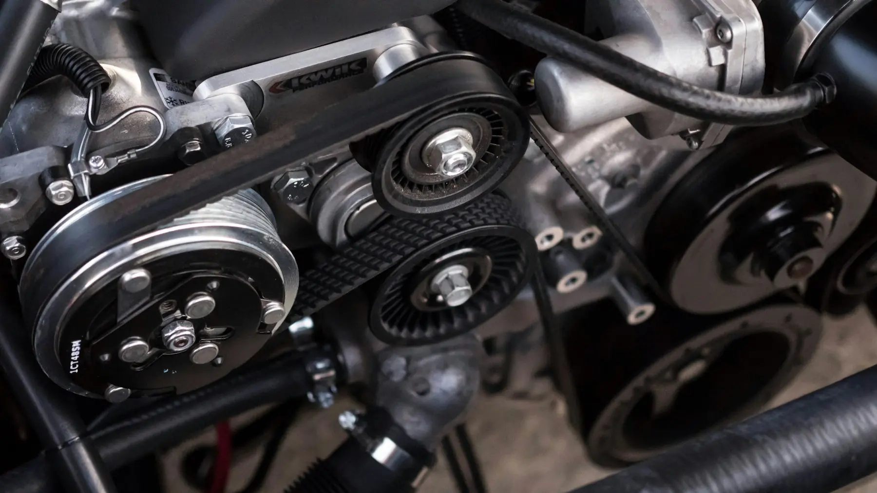 Close-up of an engine bay showing serpentine belt, pulleys and AC compressor